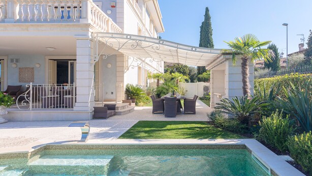 Ein Poolbereich mit gefliestem Deck, Gartenmöbeln und einer Pergola.