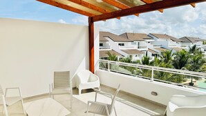 Ein Balkon mit weißen Stühlen und einem Tisch, der auf ein Wohngebiet mit Häusern und Palmen blickt.