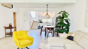 Ein modernes Wohnzimmer mit einem gelben Sessel, einem weißen Sofa, einem Essbereich mit einem Holztisch und einer Treppe, die in eine Küche führt.