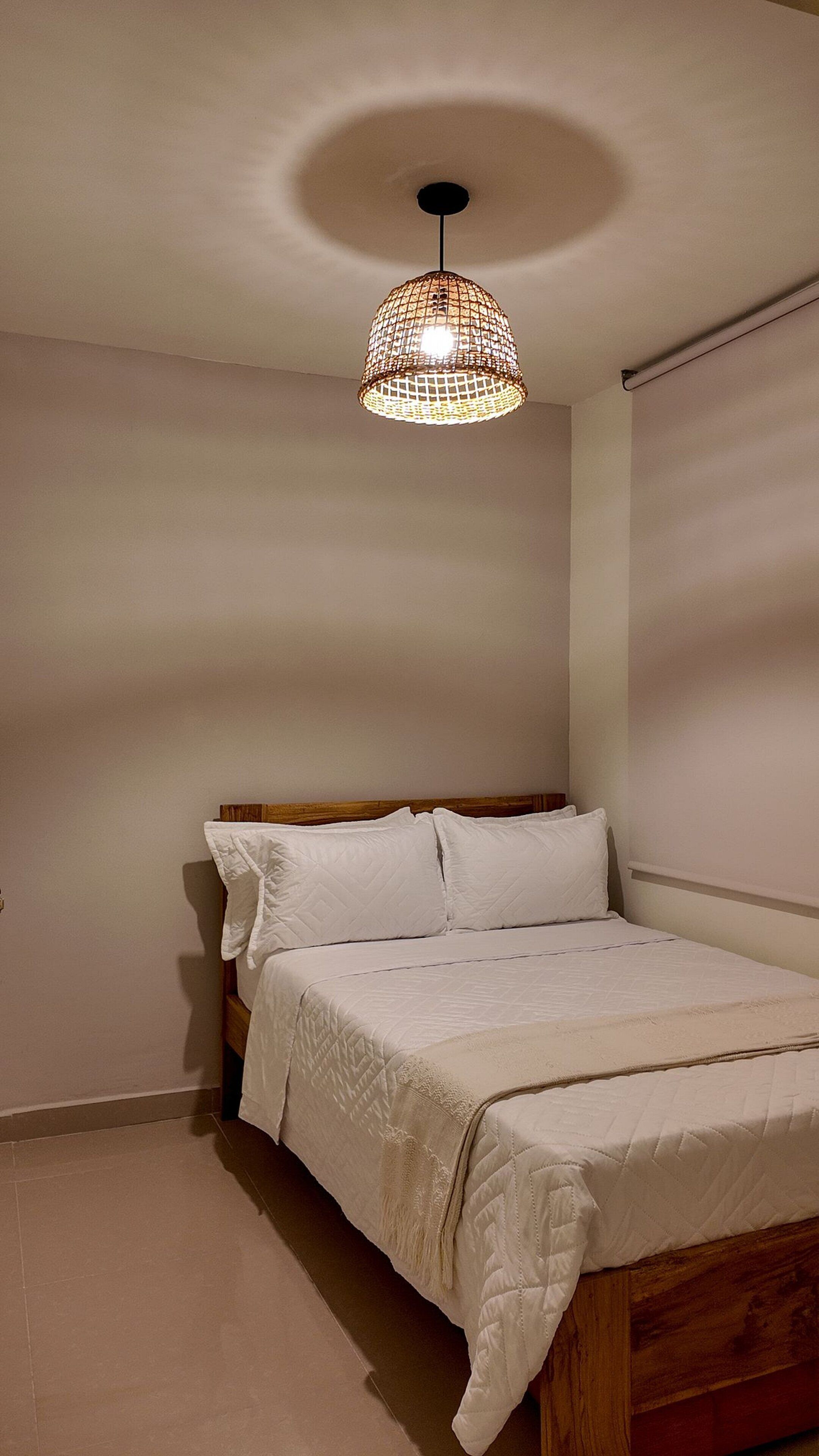 Un dormitorio con una cama de madera, ropa de cama blanca y una lámpara colgante.