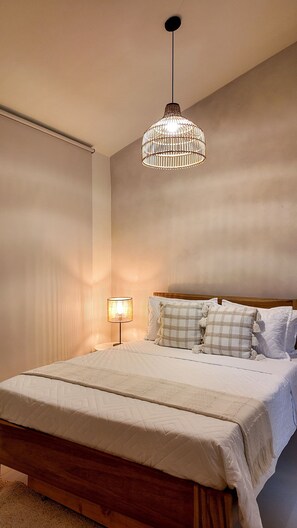 Un dormitorio con una cama, lámpara colgante, lámpara de noche y ventana con persianas.