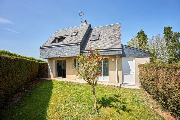 Ein modernes, zweistöckiges Haus mit geneigtem Dach, einem kleinen Garten und blauem Himmel.