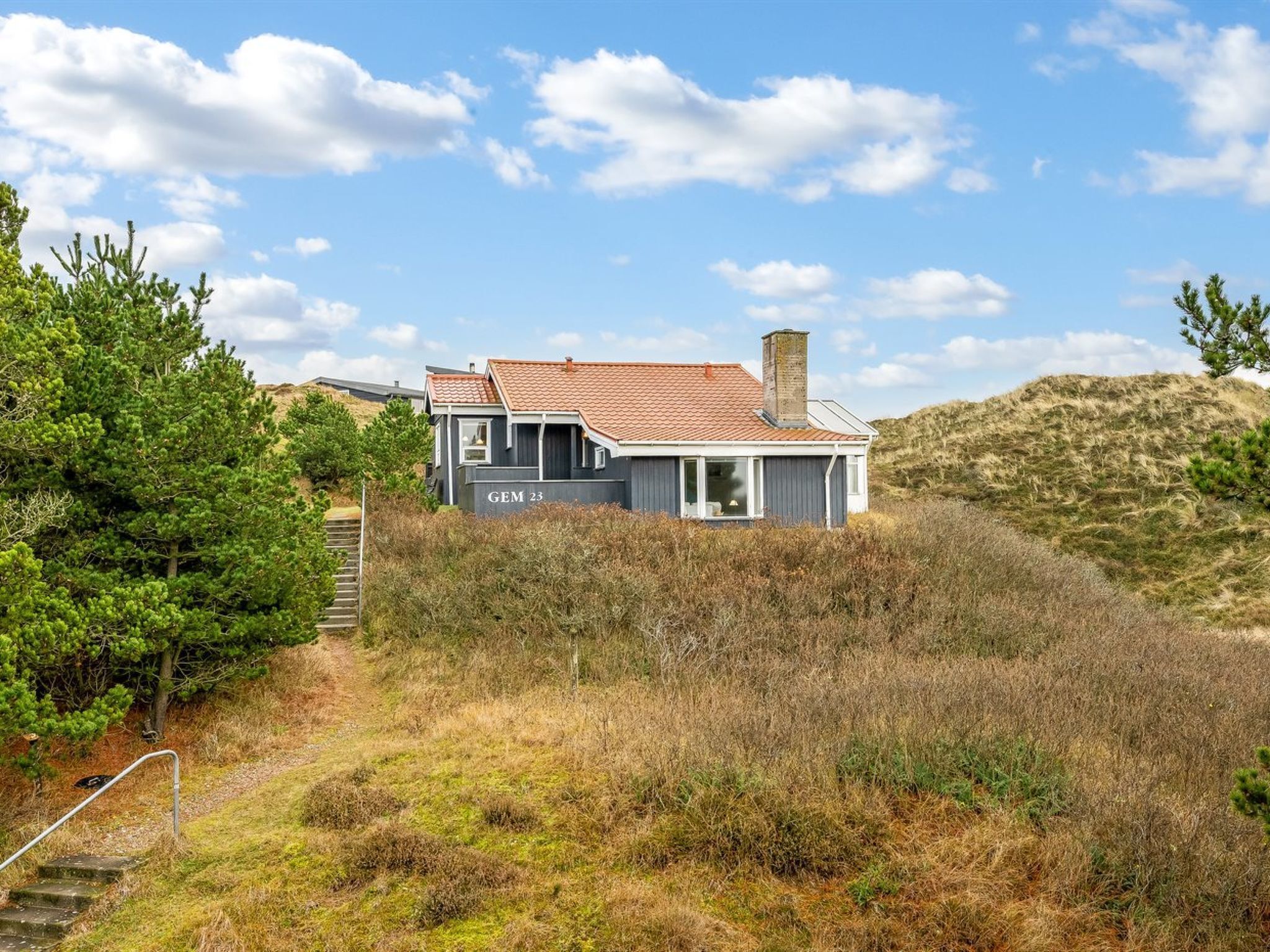 A modern house with a red-tiled roof, situated on a grassy hill with a clear sky.