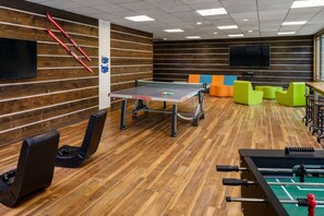 Ein Raum mit Tischtennisplatte, Kicker und farbenfroher Sitzmöbel.