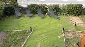 A backyard with a lawn, four lounge chairs, and a wooden fence.