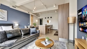 A modern living room with a sofa, coffee table, and a flat-screen TV. - Dallas Skyline Brick Loft, Sleeps 7 - Free Valet & Pool (Dallas)