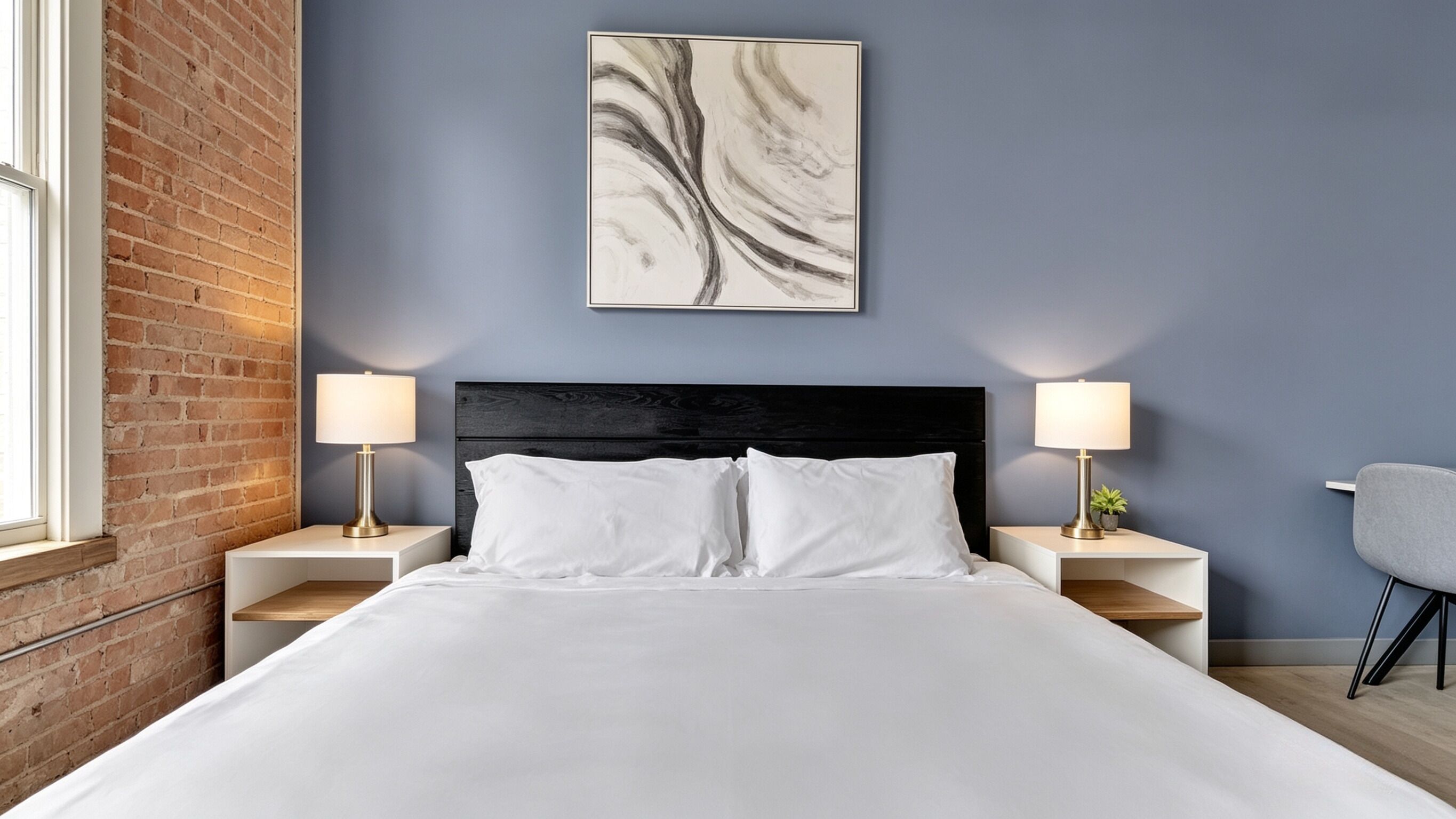 Un lit bien fait, avec du linge de lit blanc, deux tables de chevet avec des lampes, une tête de lit sombre et un seul tableau abstrait accroché au mur.