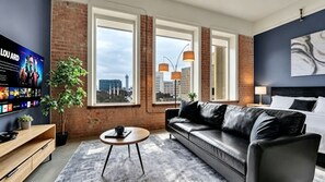 Habitación de hotel moderna con sofá de cuero, televisor de pantalla plana y ventanas amplias con vistas a la ciudad.