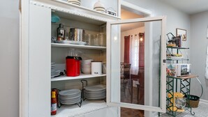 Une cuisine avec des meubles blancs, une bouilloire rouge et un four à micro-ondes posé sur une étagère verte.