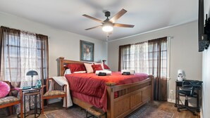Une chambre à coucher avec un lit en bois, un ventilateur de plafond, un bureau et une chaise.