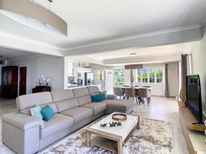 A spacious living area with a large beige sectional sofa, a coffee table, and a dining area with a table and chairs. - Villa Baradaye by Atlantic Holiday (Estreito Calheta)