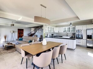 A spacious living area with a dining table and chairs, a sofa, and a kitchen with white cabinets and modern appliances. - Villa Baradaye by Atlantic Holiday (Estreito Calheta)
