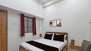 Une chambre d’hôtel comprenant un lit, une table de chevet, une chaise, une fenêtre avec des rideaux et des œuvres d’art murales.