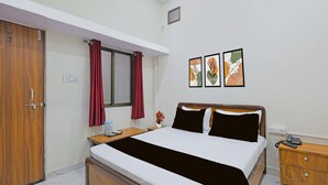 Une chambre d’hôtel comprenant un lit, une table de chevet en bois, un bureau avec une chaise, une armoire et une fenêtre avec des rideaux.