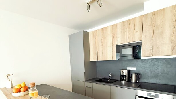 A modern kitchen with grey cabinets, a black countertop, and a wooden floor. - Modern Apartment with Terrace & Parking in Prague – Žižkov (Prague 3)