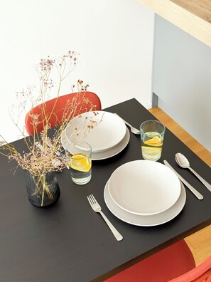 A dining table set with white plates, cutlery, and a vase with dried flowers. - Modern Apartment with Terrace & Parking in Prague – Žižkov (Prague 3)