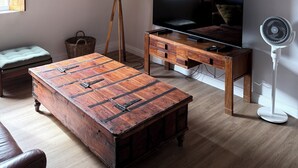 A living room with a wooden coffee table, a TV on a wooden stand, a wicker basket, a floor lamp, and a wall clock. - Peaceful 2-bedroom apartment in charming Mossel Bay perfect for relaxing (Mossel Bay)