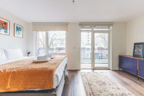Ein Schlafzimmer mit Bett, Kommode, Teppich und Blick ins Freie.