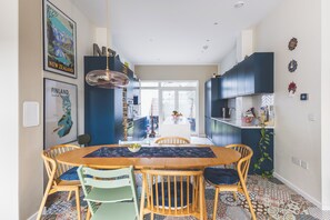 A modern kitchen with dark cabinetry, a central island, and a dining area with a wooden table and chairs. - Stylish 4BDR Home Near South Acton With Parking (Greater London)