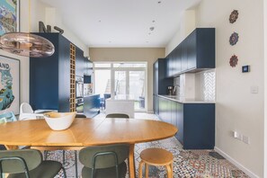 Une cuisine moderne avec des meubles de couleur sombre, une table à manger en bois et un sol à motifs.