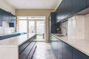 A modern kitchen with dark cabinets, a large island, and a herringbone tile backsplash. - Stylish 4BDR Home Near South Acton With Parking (Greater London)