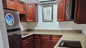 A kitchen with wooden cabinets, a stainless steel refrigerator, granite countertops, and an air conditioning unit. - 106 Deluxe Studio Suite in waterfront hotel in Singer Island, FL (Riviera Beach)