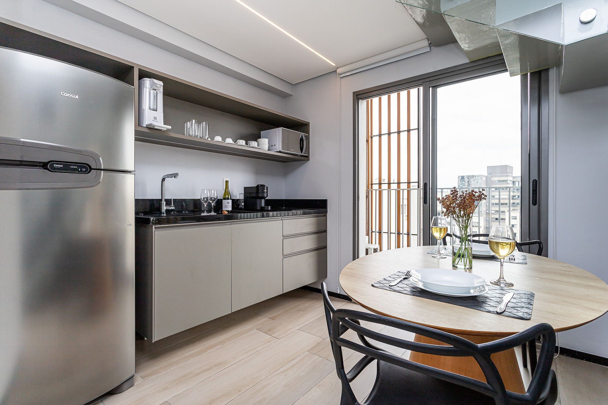Eine moderne Küche mit integriertem Kühlschrank, Mikrowelle und Kaffeemaschine. Ein Esstisch mit Stühlen, eine Vase mit Blumen und Weingläsern sind ebenfalls vorhanden.