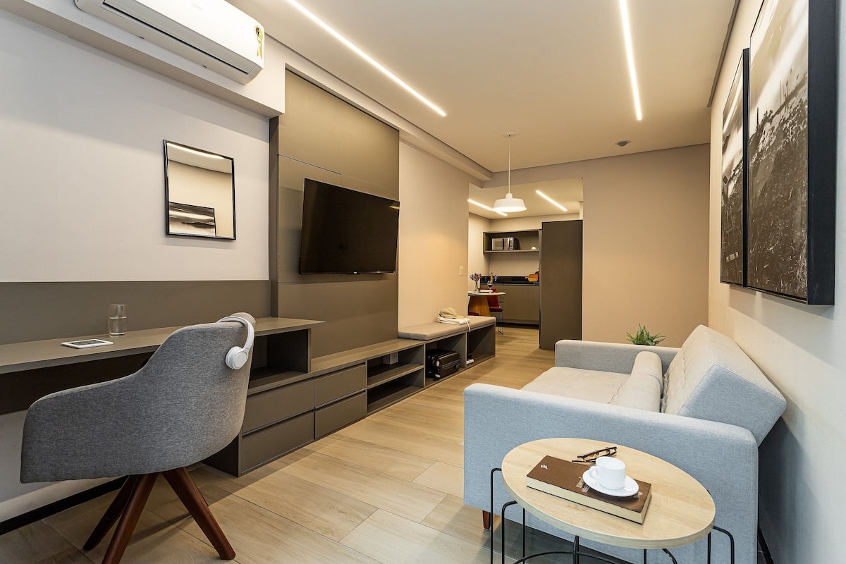 Una sala de estar moderna con un sofá, una mesa de comedor, un televisor y una cocina al fondo.