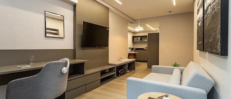 A modern living room with a sofa, a dining table, a TV, and a kitchen area in the background.