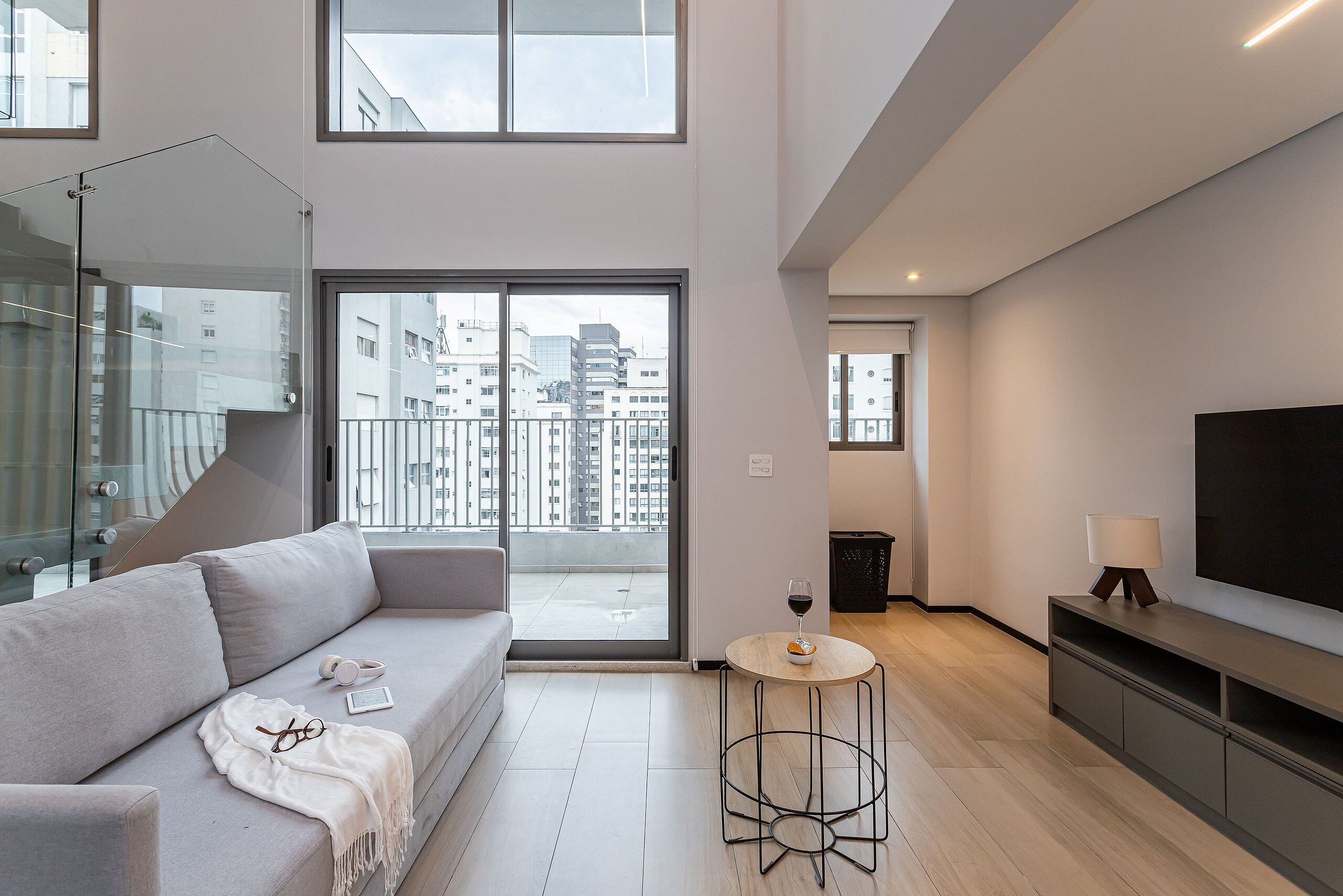 Een moderne woonkamer met een bank, een klein rond tafeltje, een televisie en een balkon met uitzicht op de stad.