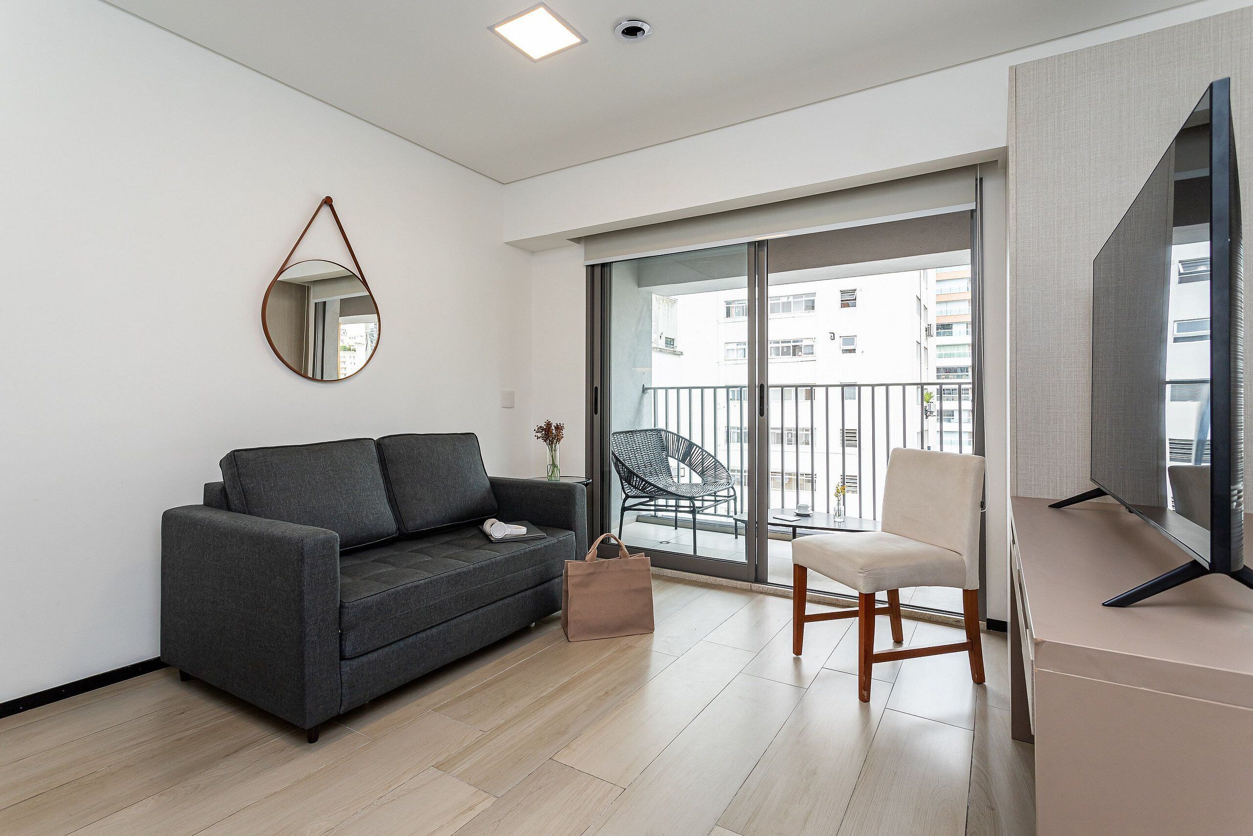 Un salon moderne avec un canapé, un fauteuil, un téléviseur, un balcon avec un fauteuil et une grande fenêtre.