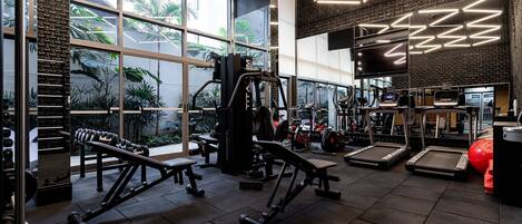 Ett gym med träningsutrustning, stora fönster och en tegelvägg.