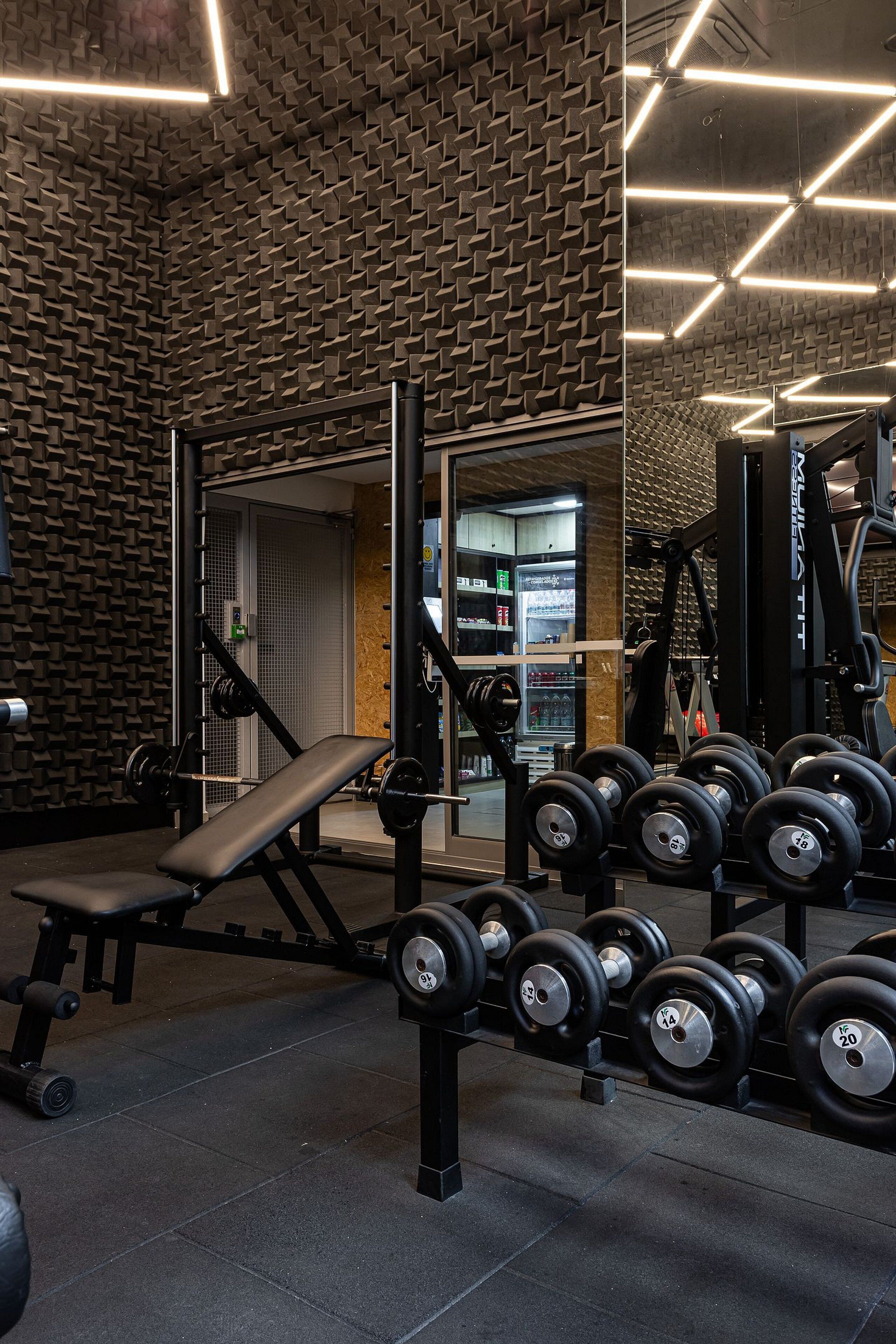 Ein Fitnessraum mit Krafttrainingsgeräten, einer Trainingsbank und einer Wand mit geometrischem Muster.