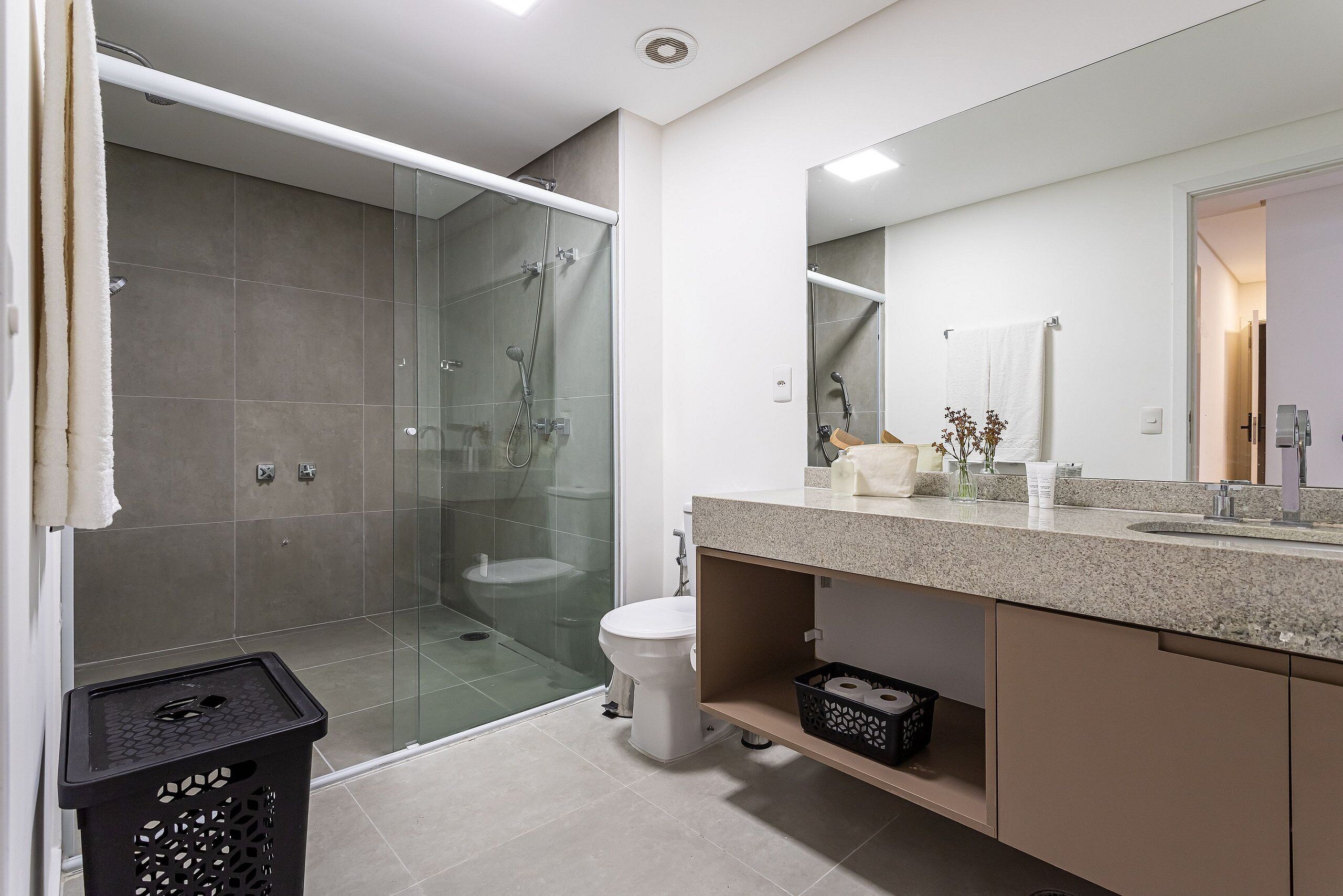 Een moderne badkamer met een glazen douchecabine, toilet, wastafel met aanrechtblad en spiegel.