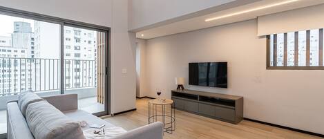 Una sala de estar moderna con un sofá, una mesita, un televisor y un balcón con vistas a la ciudad.