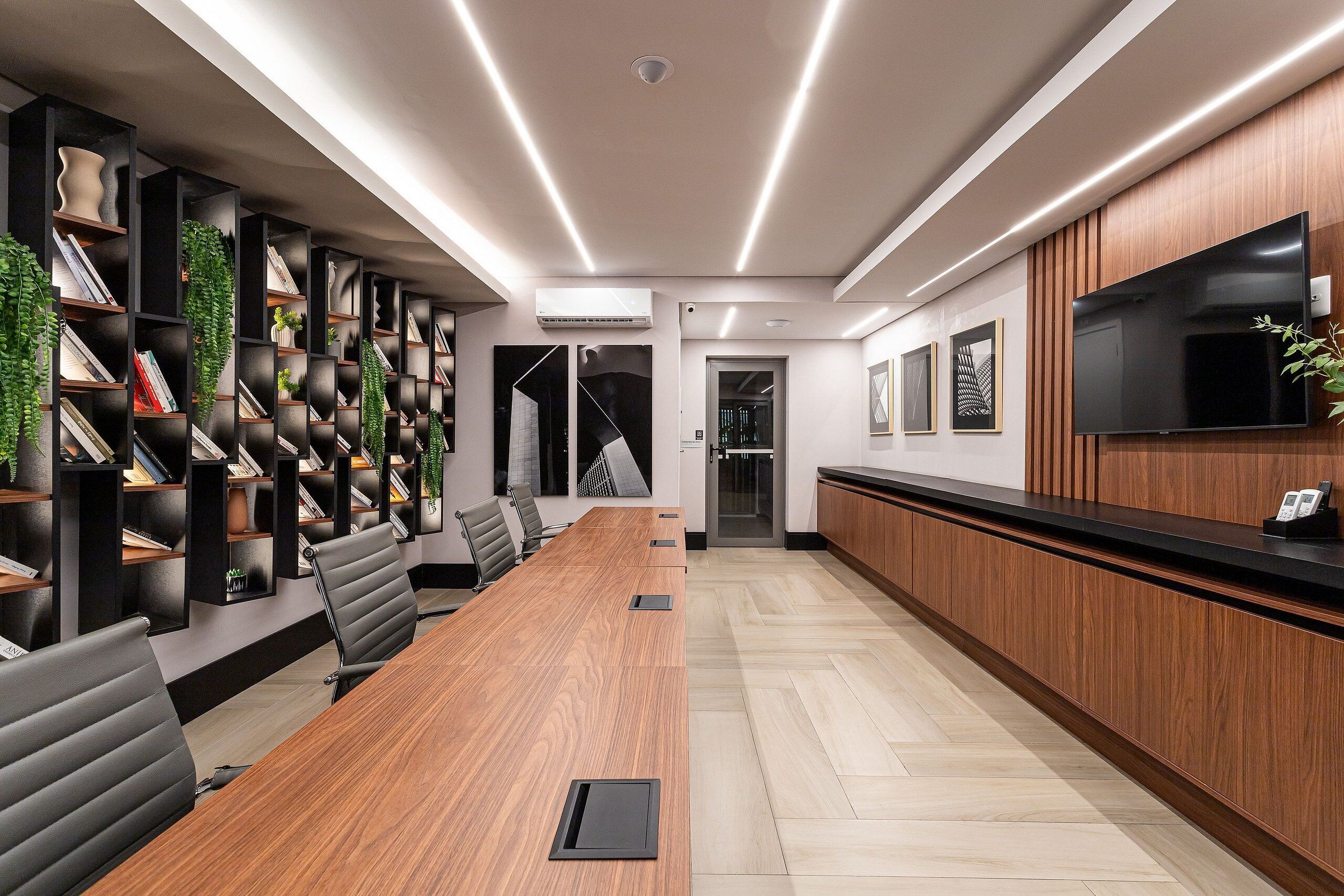 A conference room with a long table, black chairs, and a bookshelf with books and decorative items.