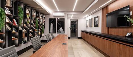 A conference room with a long table, black chairs, and a bookshelf with books and decorative items.