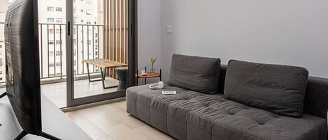 Een moderne woonkamer met een bank, een flatscreen-televisie en een balkon met uitzicht op gebouwen.