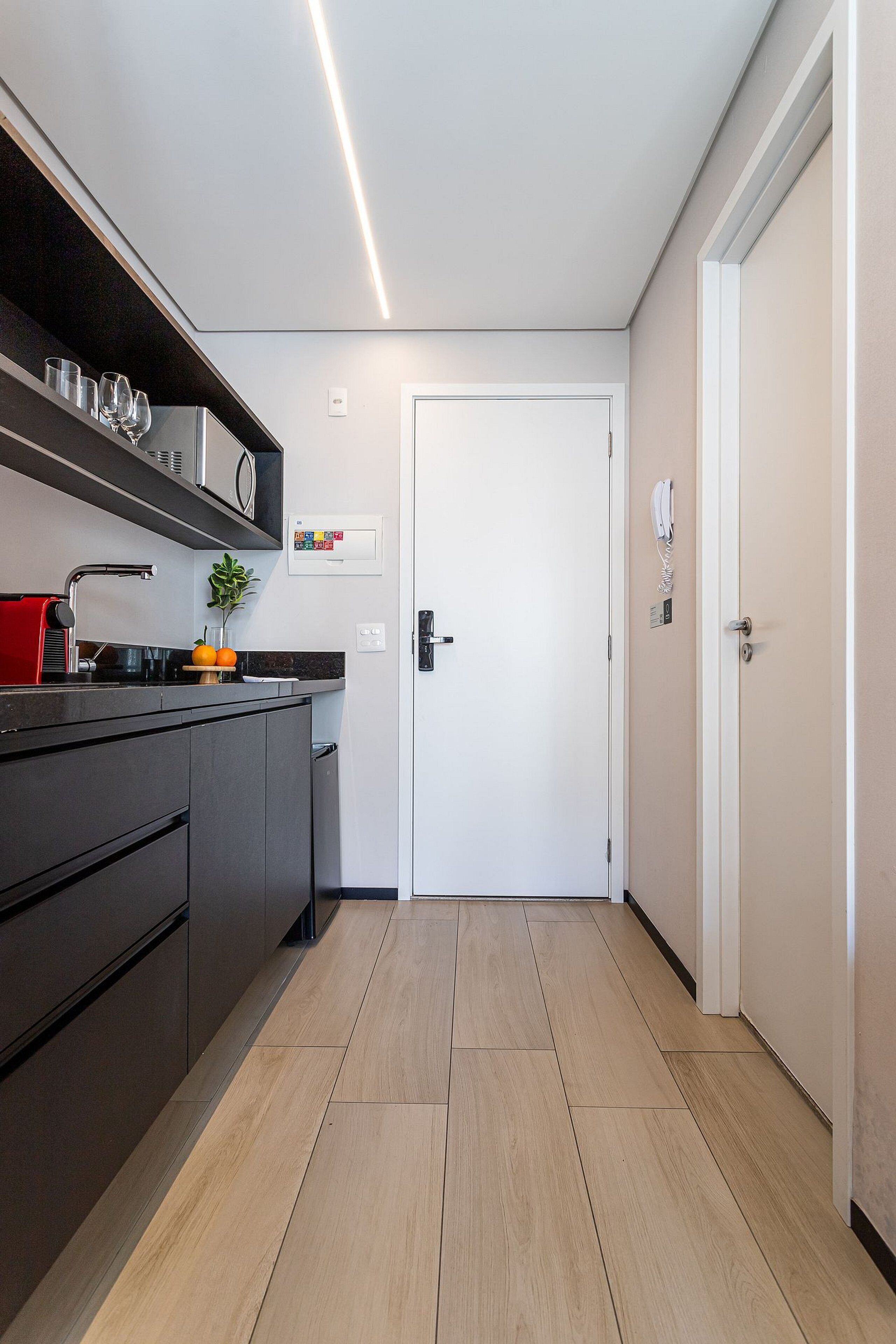 Cozinha moderna com armários escuros, bancada e porta que dá para outro cômodo.