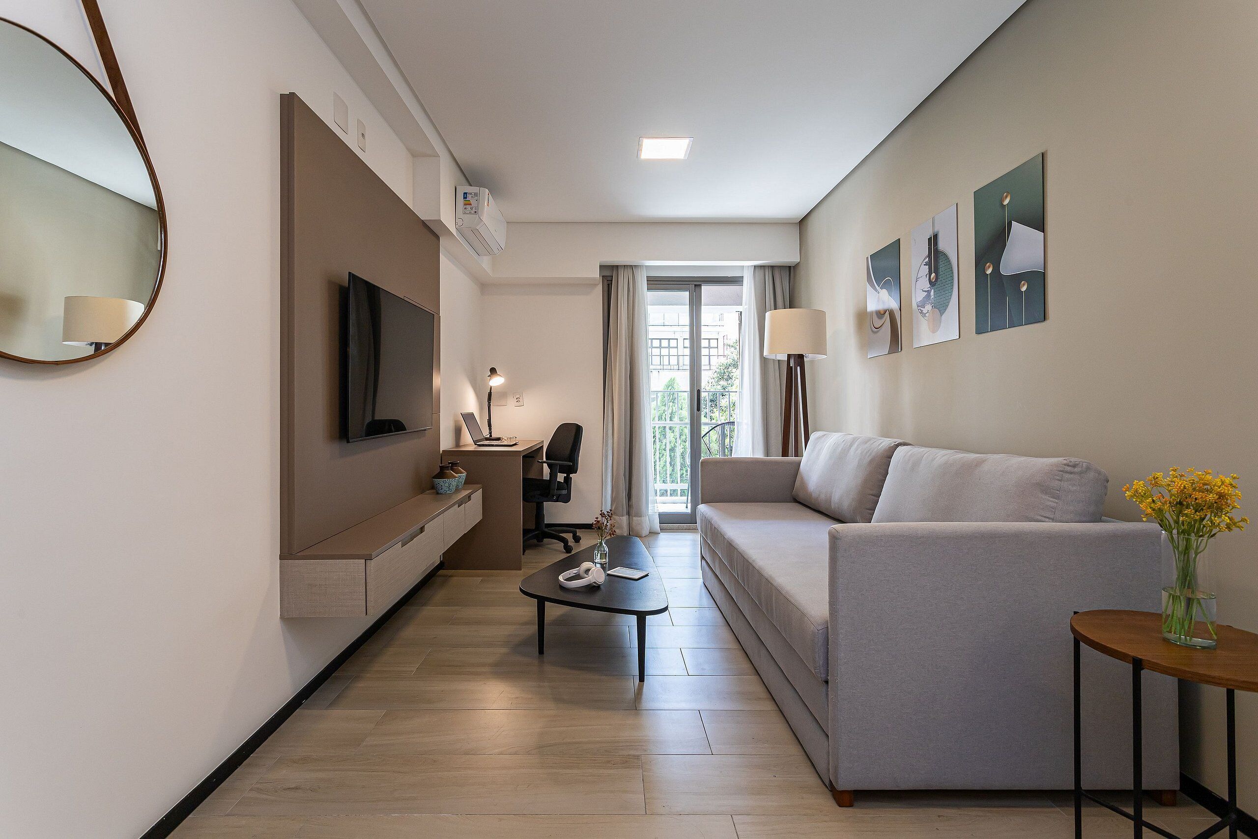 A modern hotel room with a flat-screen TV, a sofa, a small table, and artwork on the walls.
