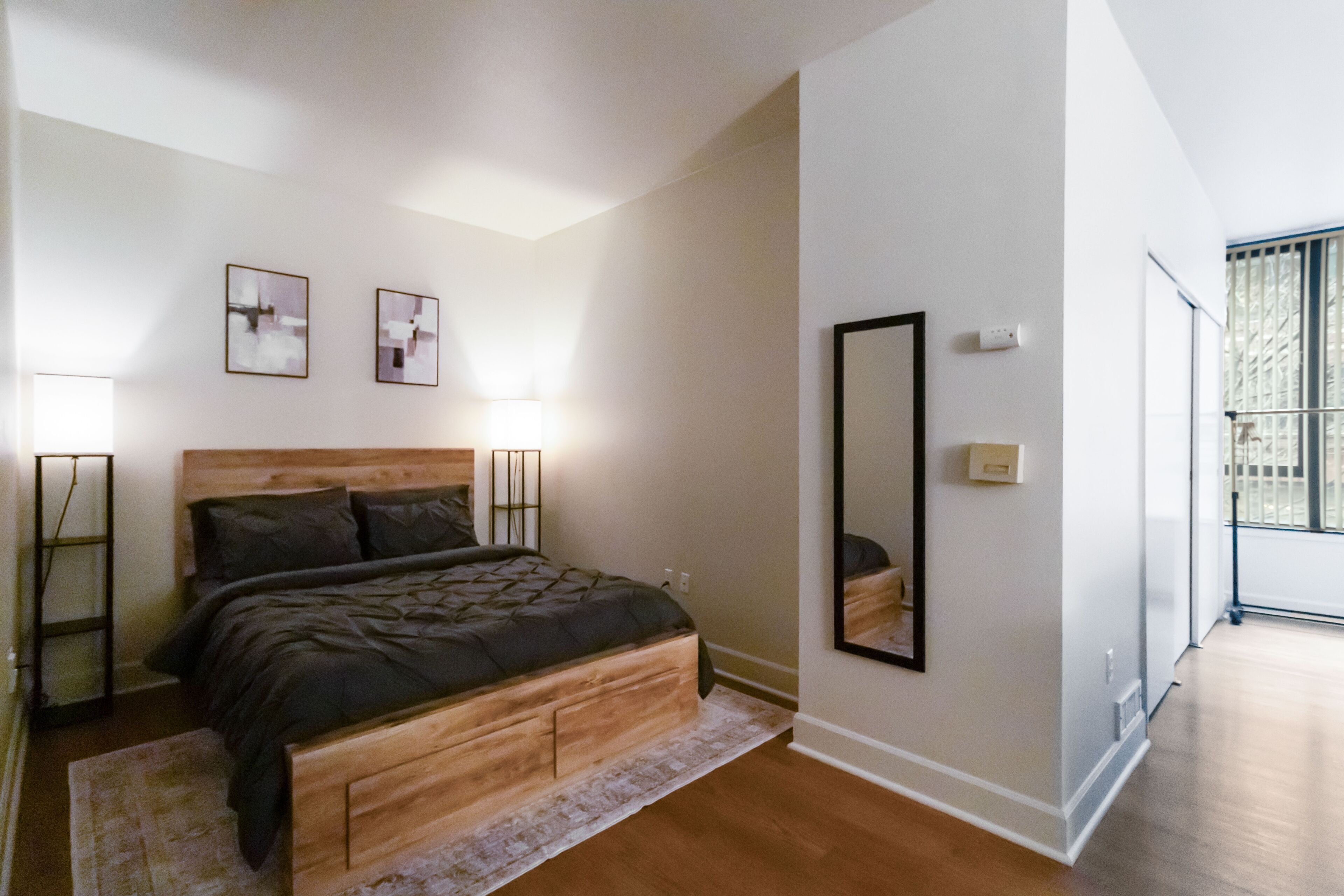 Un dormitorio con cama de madera, lámparas de noche, un espejo grande y vistas al exterior.