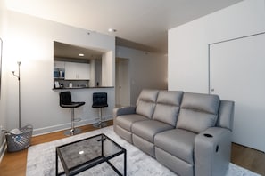 A modern living room with a grey sofa, a glass coffee table, and a kitchen area visible through an archway. - 
Luxury studio-Heart of Seattle (Seattle)