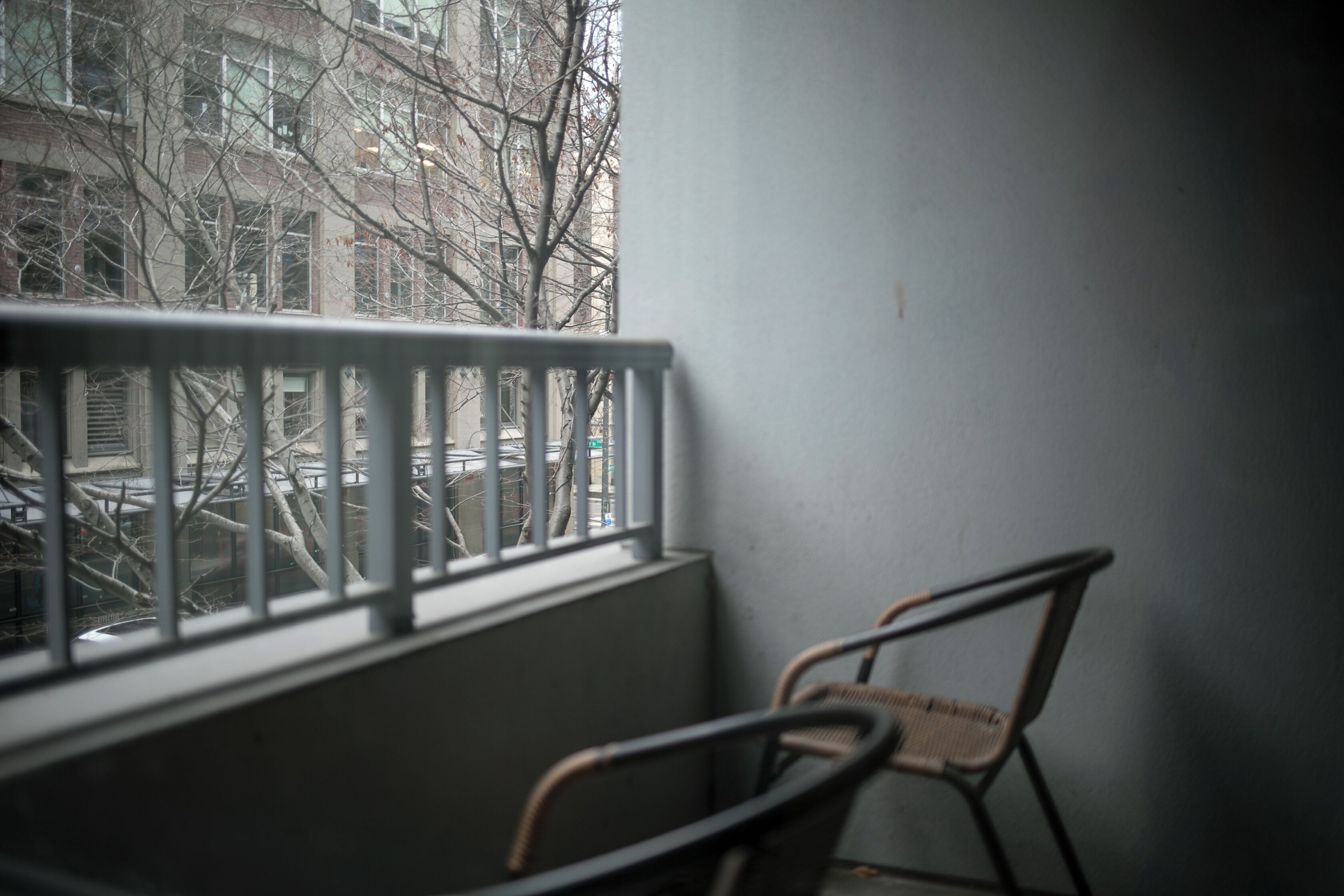Un balcon avec une rambarde en métal, une chaise et une vue sur des immeubles et des arbres sans feuilles.