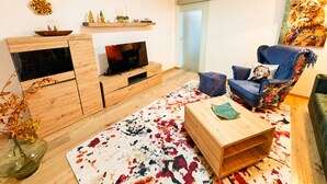 Un salon moderne avec un téléviseur, des meubles en bois, un tapis coloré et un fauteuil bleu.