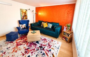 A living room with a blue armchair, teal sofa, and a colorful rug. - New - Stylish granny apartment with modern living comfort on 65 sqm (Oberschönau)