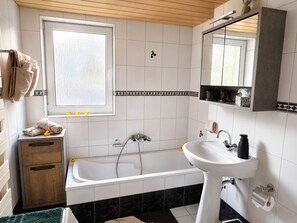 A bathroom with a bathtub, a sink, a wooden cabinet, a window, and a mirror.