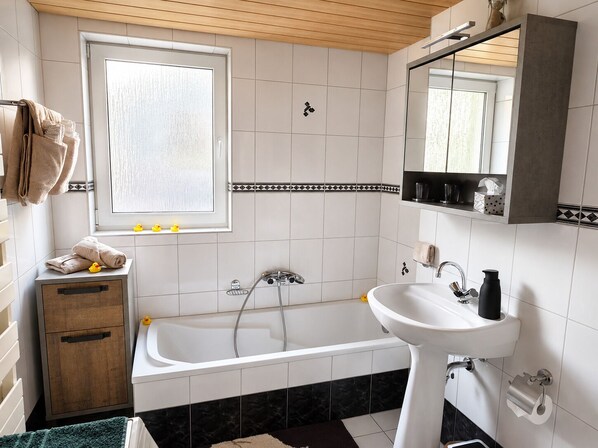 Un baño con bañera, lavamanos, un armario de madera, una ventana y un espejo.
