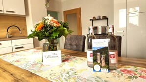 Une table à manger recouverte d’une nappe à motifs floraux, deux bouteilles de vin, un vase rempli de fleurs et un panneau avec du texte.