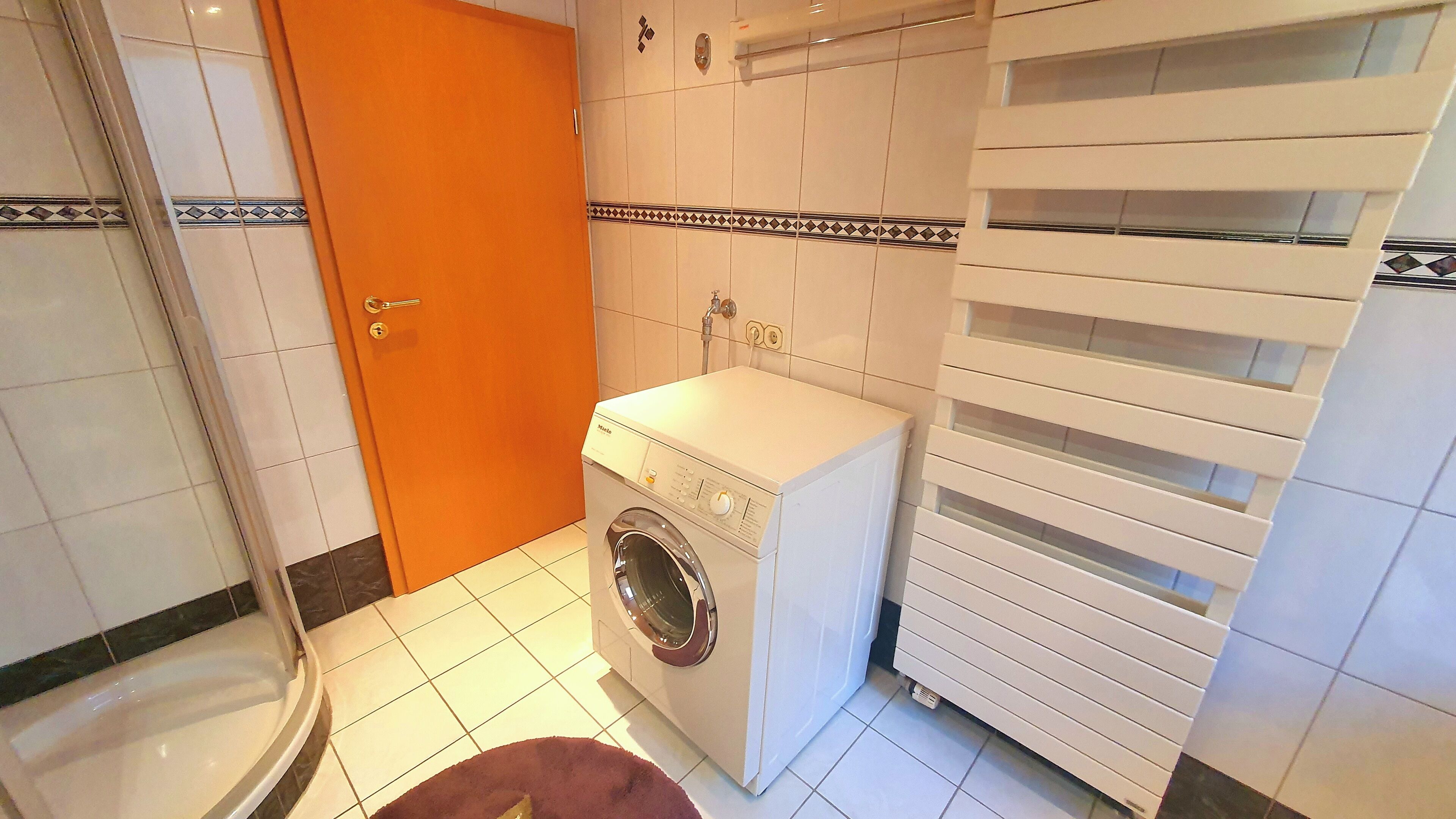 A compact bathroom with a washing machine, a toilet, and a towel rack.