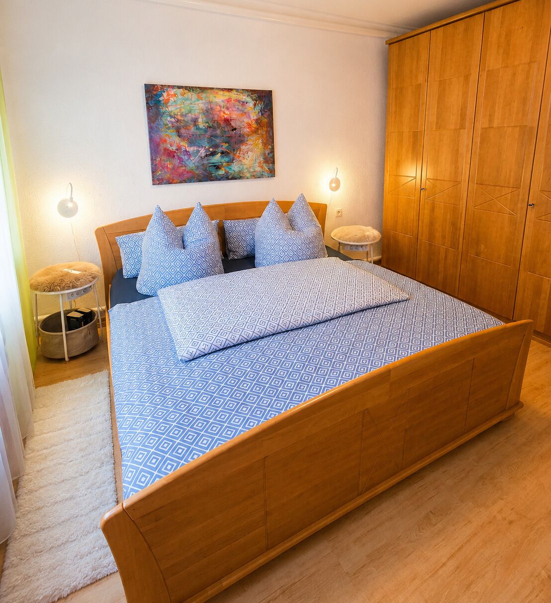 Un dormitorio con cama de madera, ropa de cama estampada, un cuadro abstracto de colores y un armario.